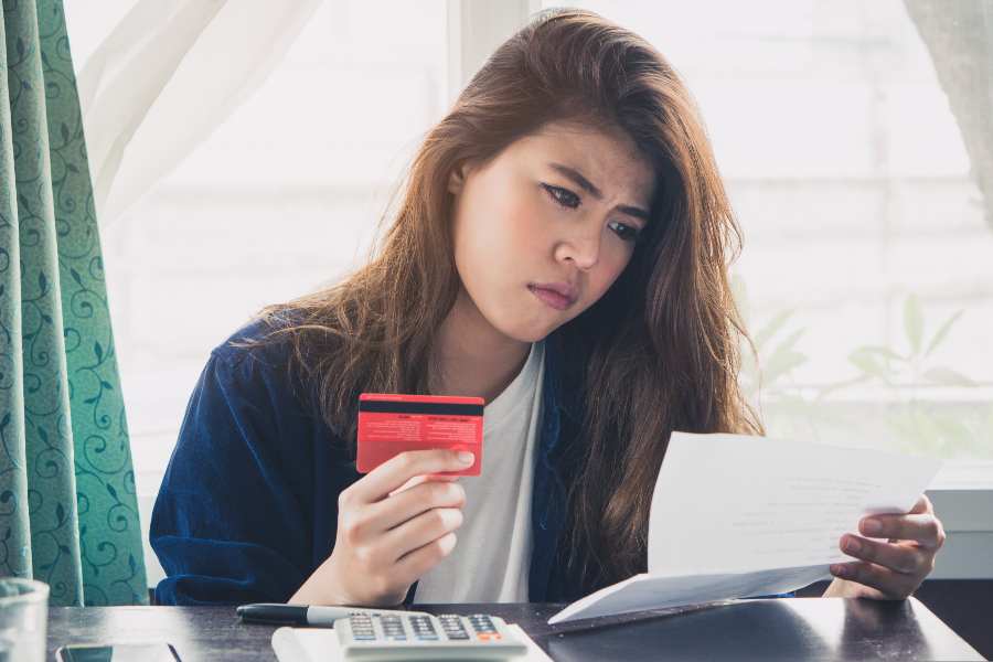 一个困惑的女人拿着一张信用卡，另一只手拿着一张账单。