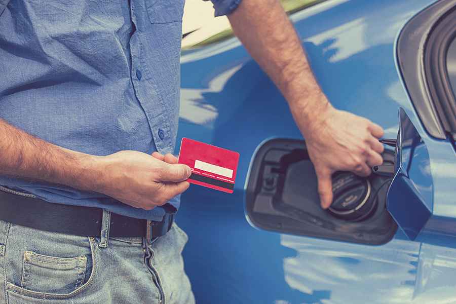 一名男子拿着燃料卡旁边的一辆蓝色汽车。