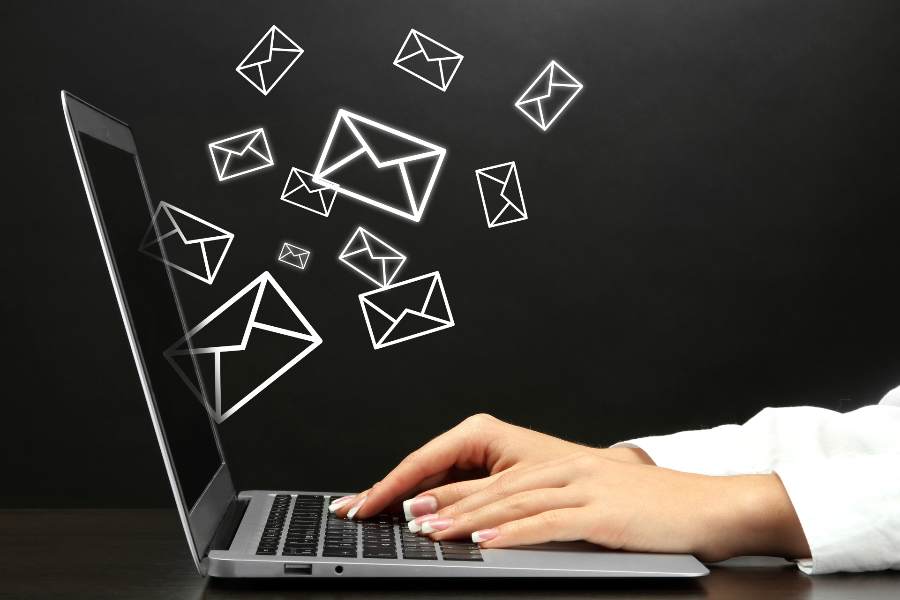 女人手在笔记本电脑上打字，一些电子邮件图标从屏幕上飞出。